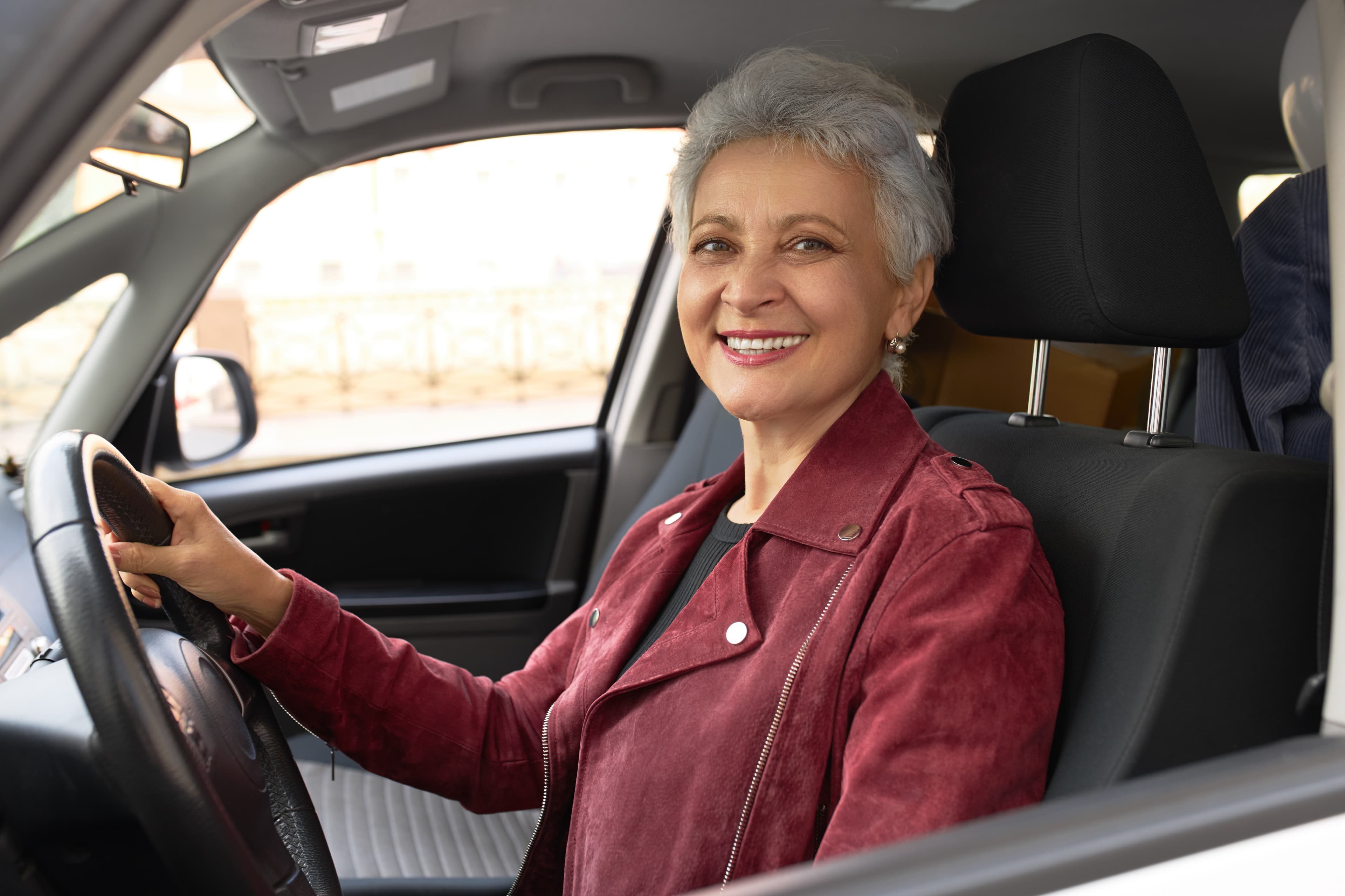 Driver in a maroon jacket smiling at the wheel of her car